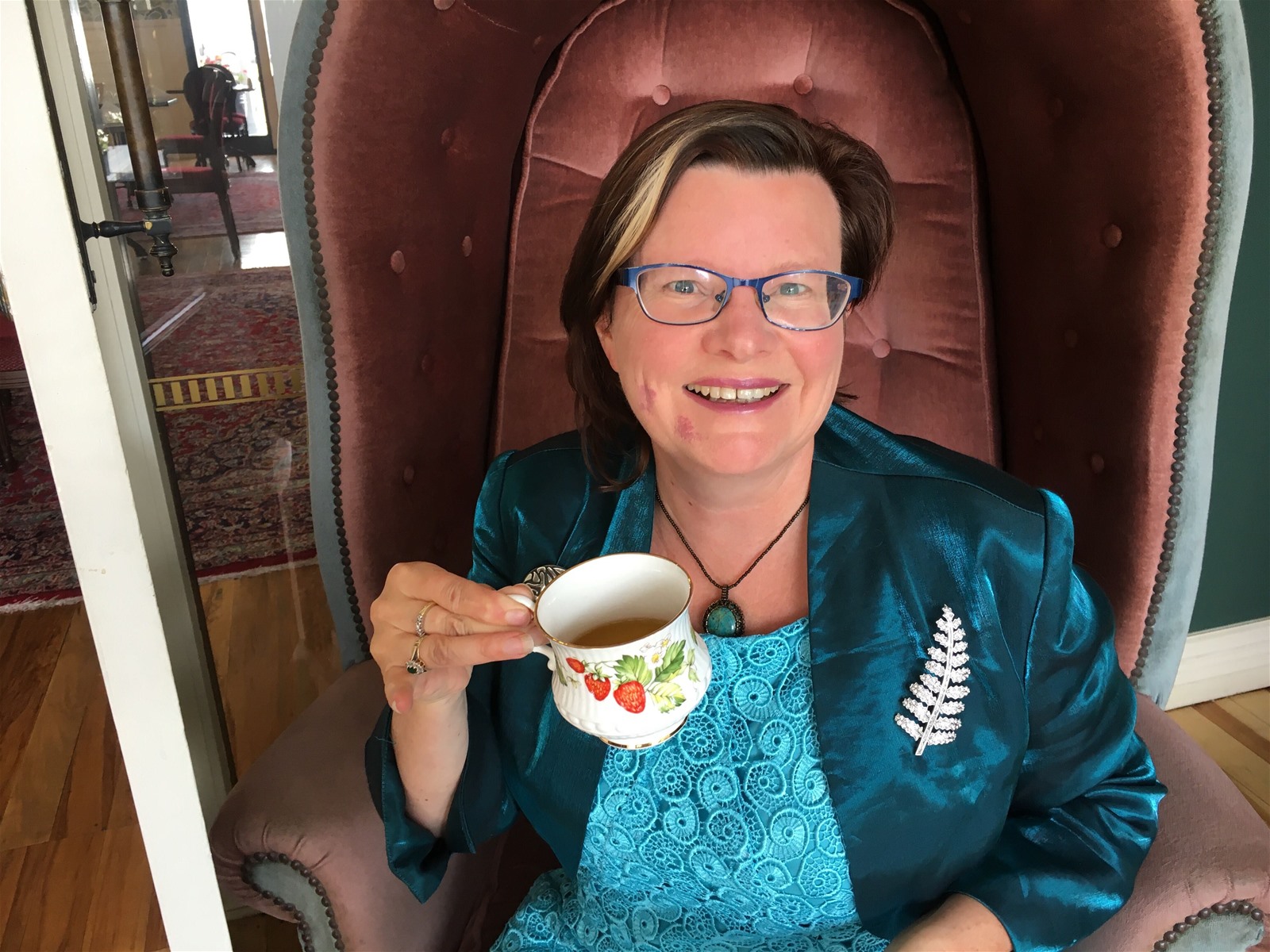 Dr Julia Anne sitting in a chair with a cup of tea, smiling