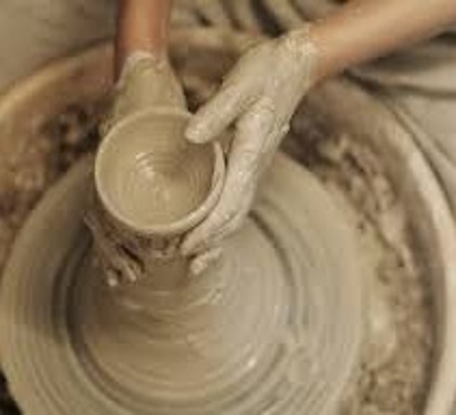 Clay covered hands at a pottery wheel spinning a clay vase